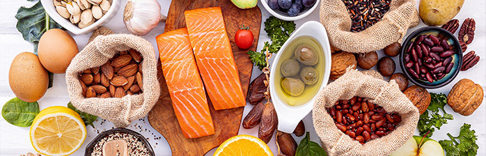 Whole foods on white countertop. Salmon, almonds, eggs, olives, vegetables.